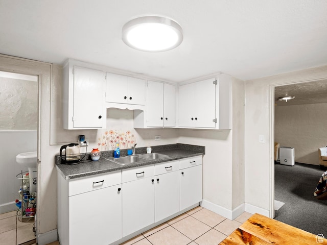 kitchen with white cabinets, dark countertops, a sink, and light tile patterned flooring