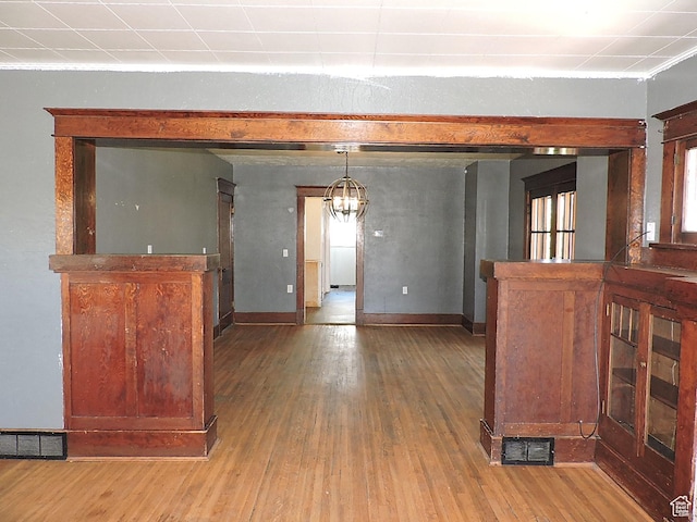 interior space featuring wood-type flooring, visible vents, baseboards, and a notable chandelier