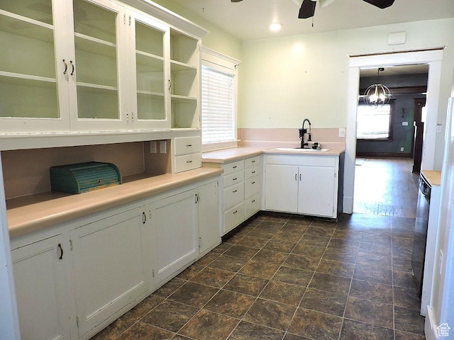 kitchen featuring a ceiling fan, a sink, glass insert cabinets, light countertops, and white cabinets