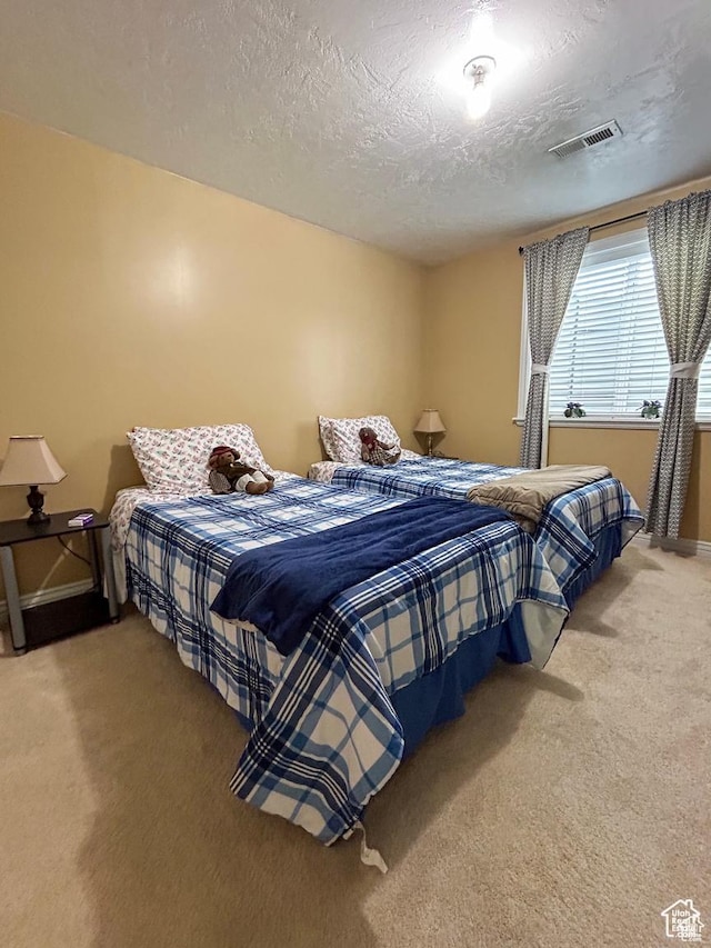 bedroom with light carpet, a textured ceiling, visible vents, and baseboards