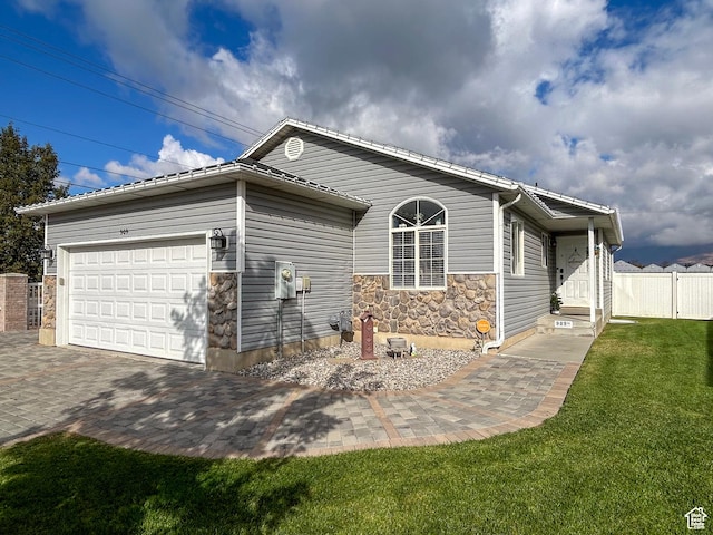 view of side of property featuring fence, an attached garage, driveway, stone siding, and a lawn