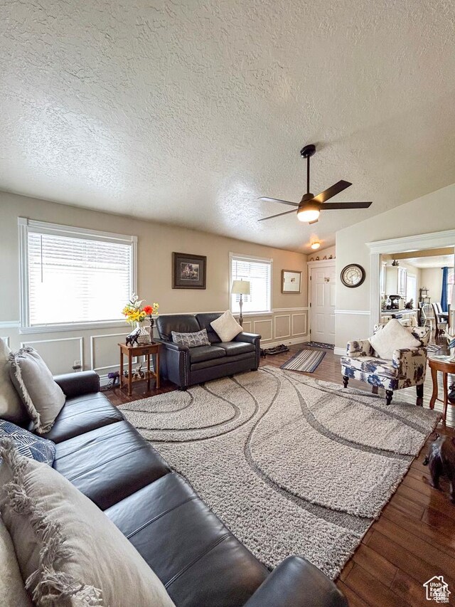 living area featuring a wainscoted wall, wood finished floors, a decorative wall, a textured ceiling, and ceiling fan