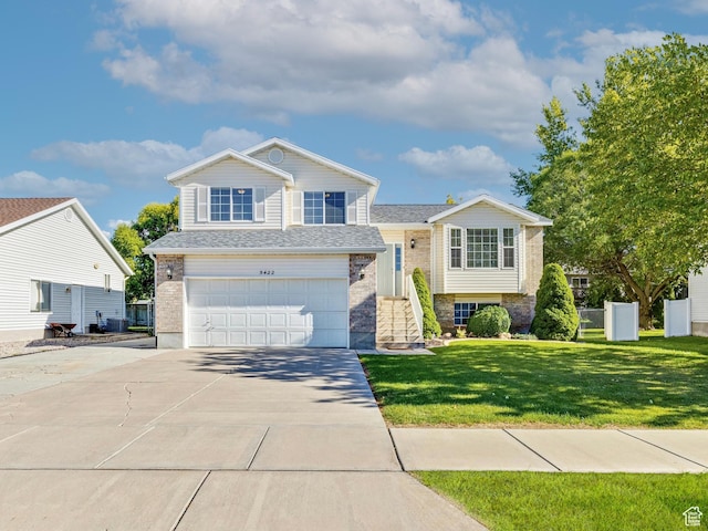 tri-level home featuring a garage, brick siding, a front yard, and concrete driveway