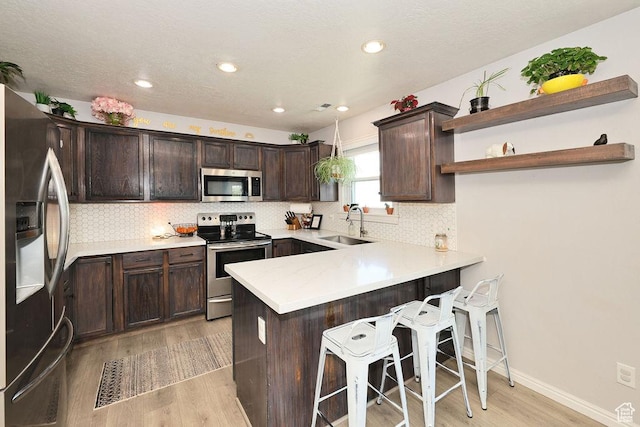 kitchen with dark brown cabinets, a sink, light wood-type flooring, a peninsula, and appliances with stainless steel finishes