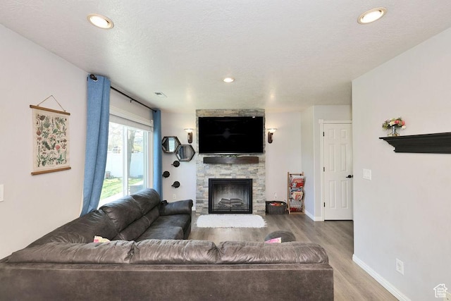 living area featuring visible vents, baseboards, recessed lighting, wood finished floors, and a stone fireplace