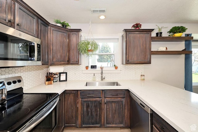 kitchen with stainless steel appliances, open shelves, dark brown cabinets, a healthy amount of sunlight, and a sink