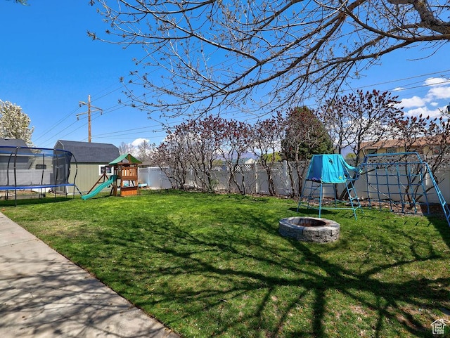 view of yard with a fire pit, a trampoline, a fenced backyard, and a playground