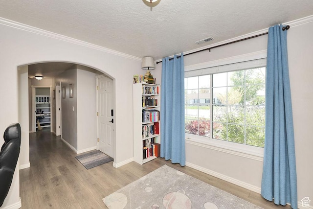foyer entrance featuring wood finished floors, a textured ceiling, arched walkways, baseboards, and visible vents