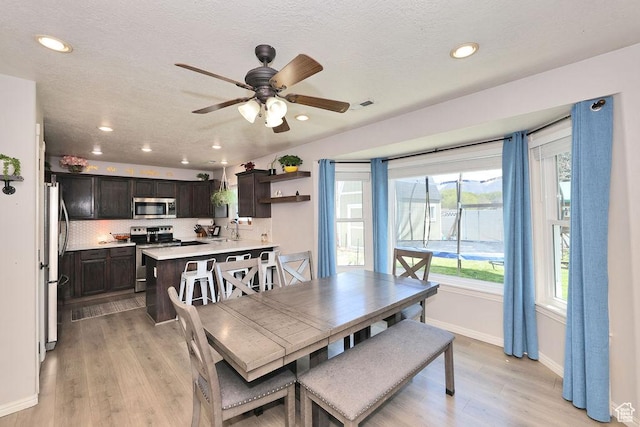 dining room with light wood-type flooring, a ceiling fan, baseboards, and a wealth of natural light