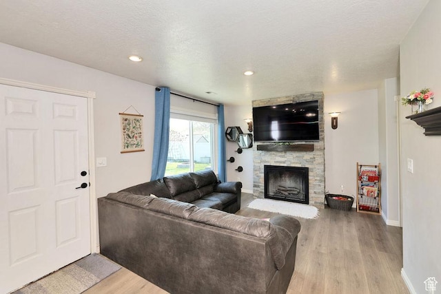 living area featuring a textured ceiling, baseboards, recessed lighting, wood finished floors, and a stone fireplace