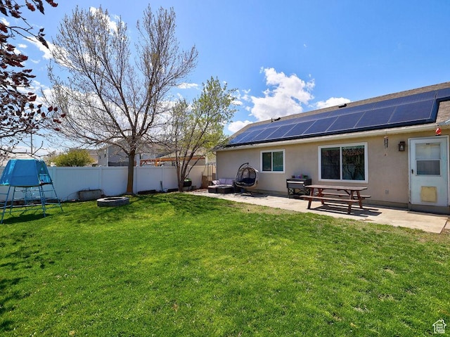 back of house with roof mounted solar panels, a fenced backyard, a yard, a patio, and an outdoor fire pit