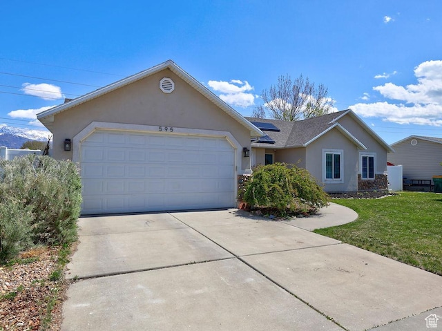 ranch-style house featuring concrete driveway, a garage, roof mounted solar panels, a front yard, and stucco siding