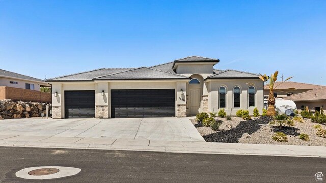 view of front of property featuring concrete driveway, stone siding, a tiled roof, an attached garage, and stucco siding