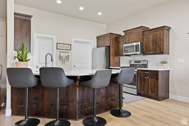 1920 W 180 N, Hurricane, UT 84737 - kitchen with light countertops, a breakfast bar area, light wood-style flooring, backsplash, and appliances with stainless steel finishes