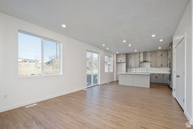 912 W Bellshill Dr Unit 15, Murray, UT 84123 - kitchen with wall chimney range hood, gray cabinets, light wood-style flooring, an island with sink, and a textured ceiling