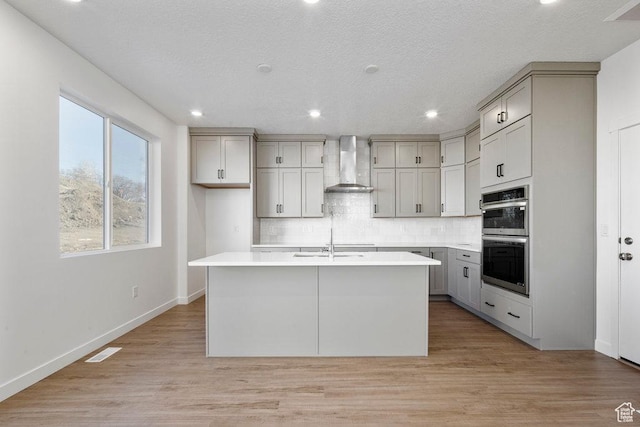 912 W Bellshill Dr Unit 15, Murray, UT 84123 - kitchen with wall chimney exhaust hood, gray cabinets, a sink, decorative backsplash, and a kitchen island with sink