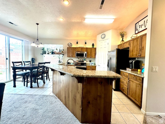 kitchen with brown cabinets, stainless steel appliances, a textured ceiling, and light tile patterned floors