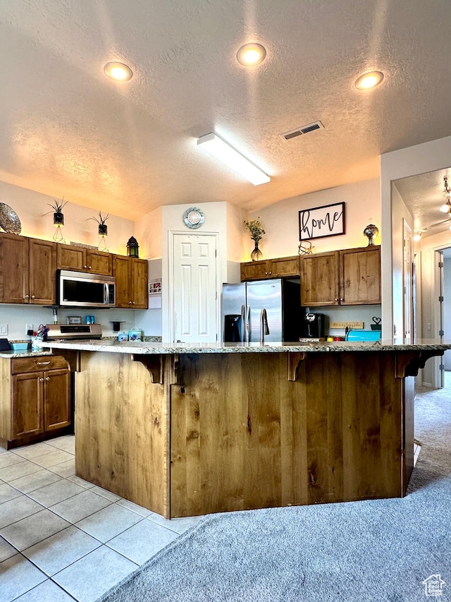 kitchen with brown cabinets, a textured ceiling, visible vents, and stainless steel appliances
