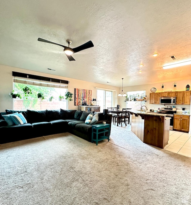 living room with a textured ceiling, a ceiling fan, light carpet, and visible vents