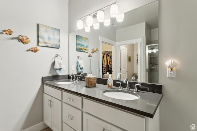 bathroom with double vanity, a shower stall, a spacious closet, and a sink