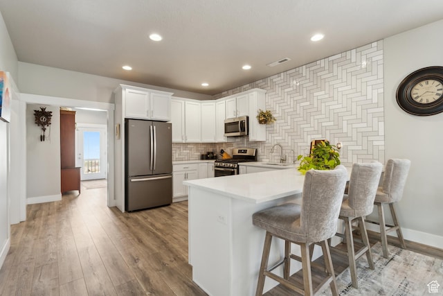 kitchen with white cabinets, a peninsula, baseboards, light countertops, and appliances with stainless steel finishes