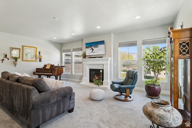 carpeted living area featuring baseboards, a glass covered fireplace, a textured ceiling, and recessed lighting