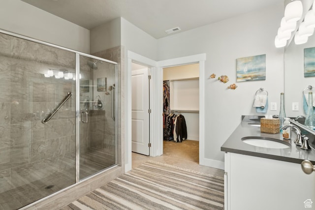 full bath with a shower stall, double vanity, visible vents, a sink, and a walk in closet