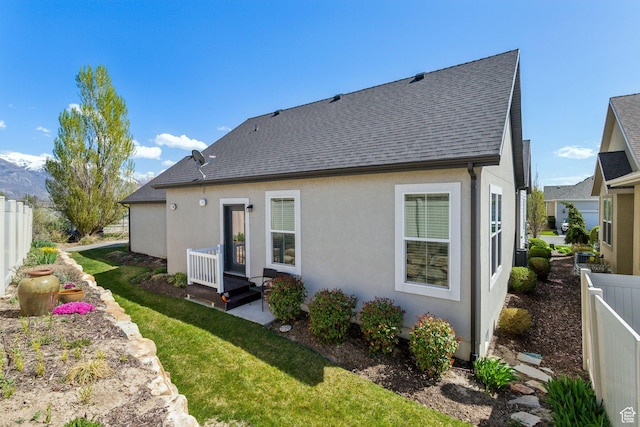 back of property with fence, roof with shingles, a yard, and stucco siding