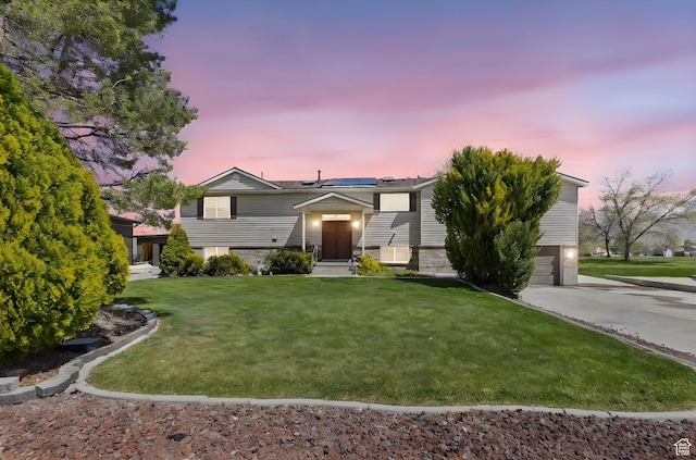 split foyer home with roof mounted solar panels, an attached garage, concrete driveway, and a front lawn