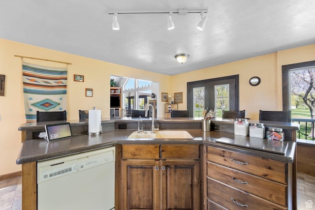 kitchen featuring dark countertops, a sink, dishwasher, brown cabinetry, and french doors