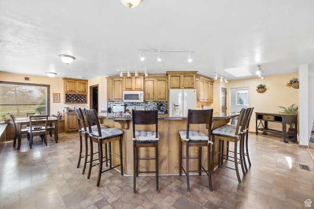 kitchen featuring visible vents, a kitchen breakfast bar, backsplash, and white appliances