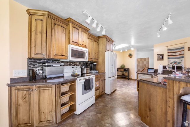 kitchen with white appliances, dark countertops, track lighting, and a sink