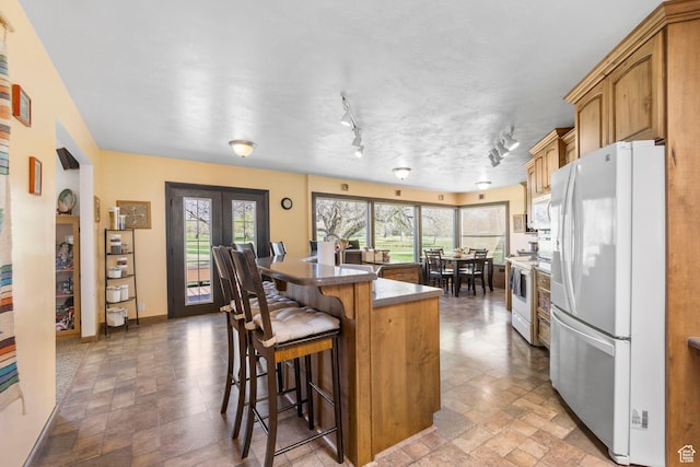 kitchen with stone finish floor, a kitchen island, a kitchen bar, dark countertops, and white appliances