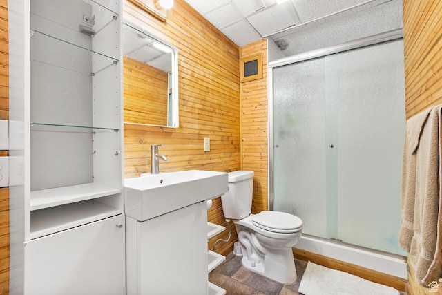 bathroom featuring a sink, a stall shower, wooden walls, and toilet