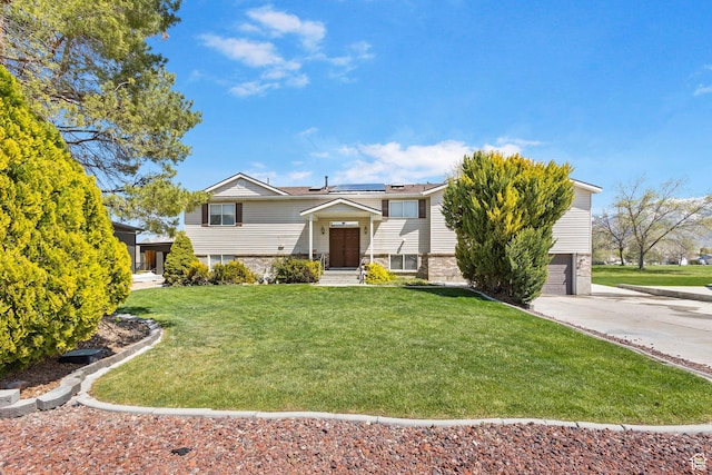 split foyer home with an attached garage, stone siding, a front yard, concrete driveway, and solar panels