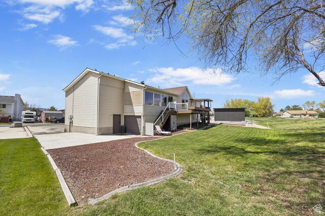 rear view of property with a garage, a deck, a lawn, driveway, and stairway