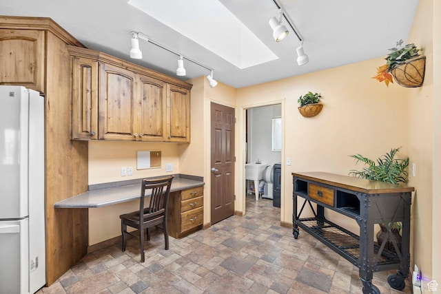 office space with track lighting, baseboards, stone finish floor, and built in desk