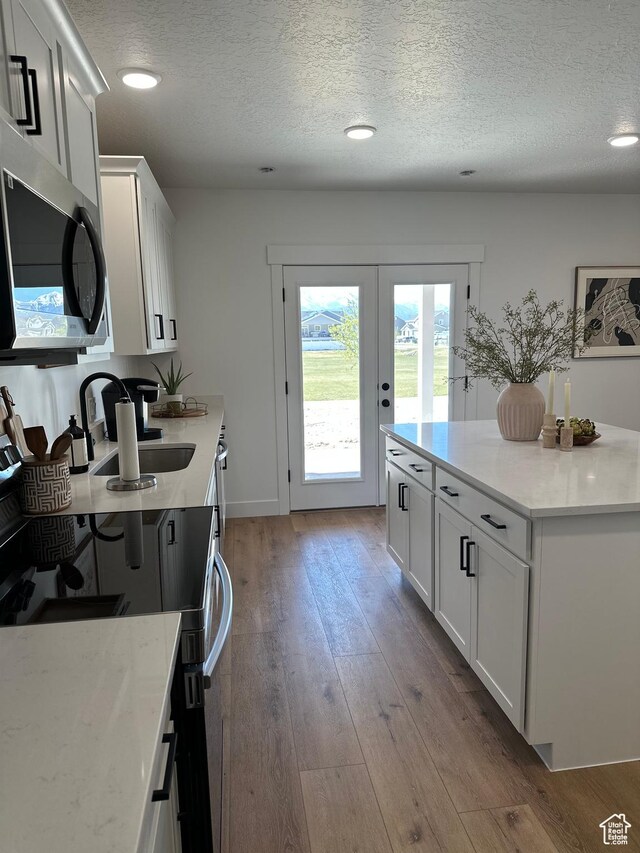 7877 Walnut Dr Unit 303, Eagle Mountain, UT 84005 - kitchen with white cabinets, a sink, a textured ceiling, stainless steel microwave, and hardwood / wood-style flooring