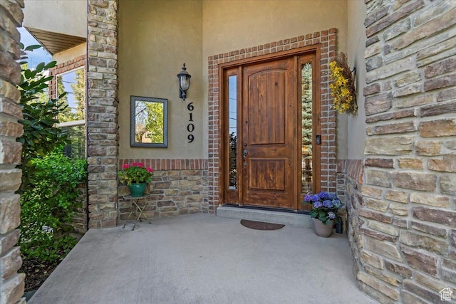 view of exterior entry with stucco siding, stone siding, and covered porch