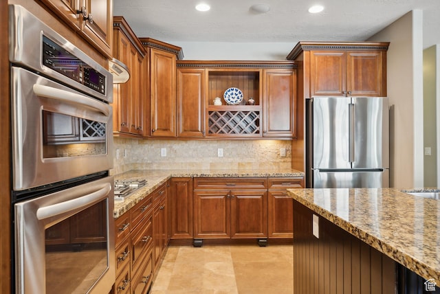kitchen with light stone counters, decorative backsplash, brown cabinets, appliances with stainless steel finishes, and recessed lighting