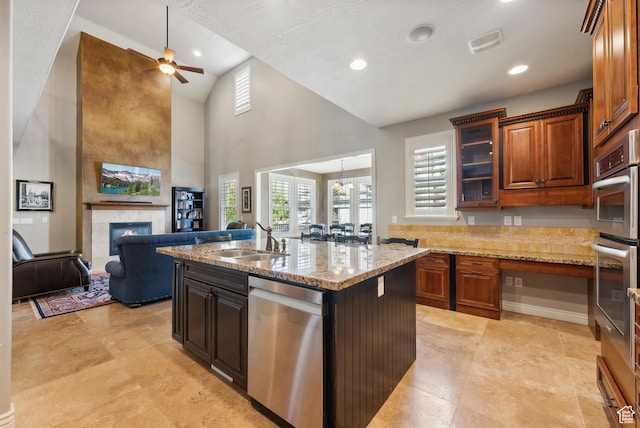 kitchen with a ceiling fan, a sink, a kitchen island with sink, a fireplace, and appliances with stainless steel finishes
