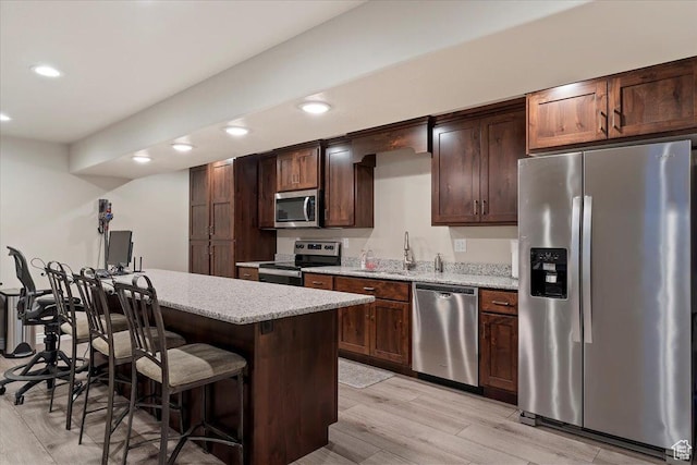 kitchen with stainless steel appliances, a sink, recessed lighting, light wood-style floors, and a breakfast bar area