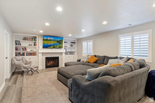 living room with recessed lighting, a lit fireplace, visible vents, and light wood-type flooring