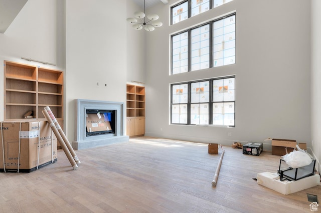 unfurnished living room featuring wood finished floors, plenty of natural light, a glass covered fireplace, a chandelier, and a high ceiling