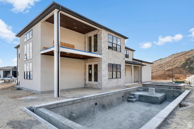 back of property featuring stucco siding, stone siding, and french doors