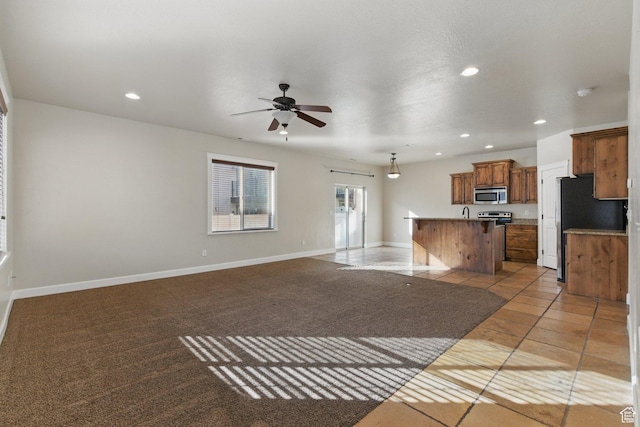 1247 N Baycrest Dr, Saratoga Springs, UT 84045 - interior space featuring a kitchen island with sink, open floor plan, a ceiling fan, brown cabinets, and appliances with stainless steel finishes