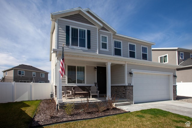 view of front of house with driveway, a porch, stone siding, and fence