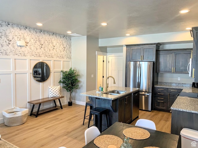 150 W Seasons Ln Unit 4, Garden City, UT 84028 - kitchen with light wood finished floors, stainless steel appliances, a sink, light stone countertops, and a center island with sink