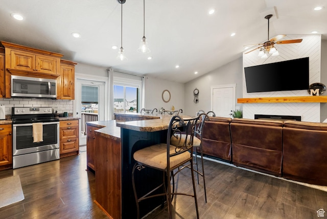 kitchen featuring a breakfast bar, vaulted ceiling, brown cabinets, and stainless steel appliances