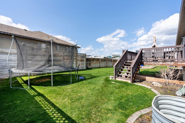view of yard featuring a fenced backyard, a deck, stairs, and a trampoline